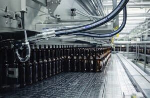 Lavadora industrial de botellas operando en línea automatizada con sensores y tuberías en planta de producción