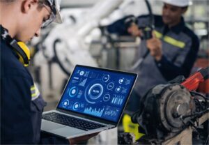 Técnico industrial con casco y auriculares analizando datos de automatización industrial en computadora portátil en fábrica